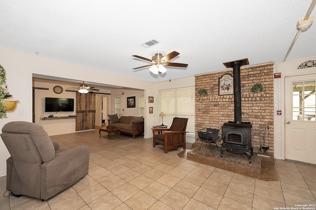 tiled living room featuring a wood stove and ceiling fan