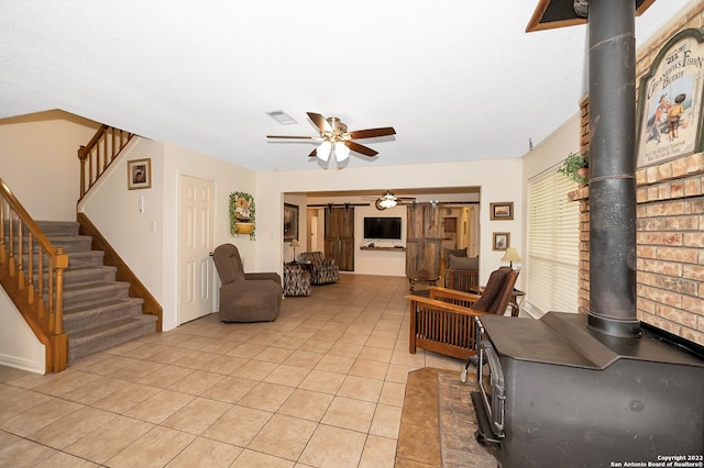 living room featuring light tile patterned flooring, ceiling fan, and a wood stove