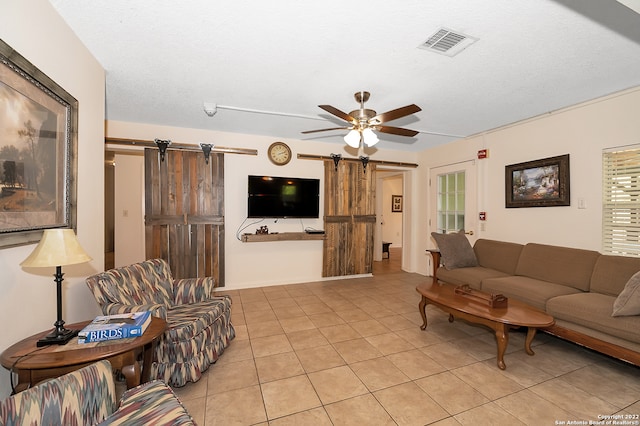 tiled living room with ceiling fan, a barn door, and a textured ceiling