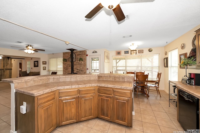 kitchen with a center island, a wood stove, dishwasher, tile countertops, and light tile patterned floors