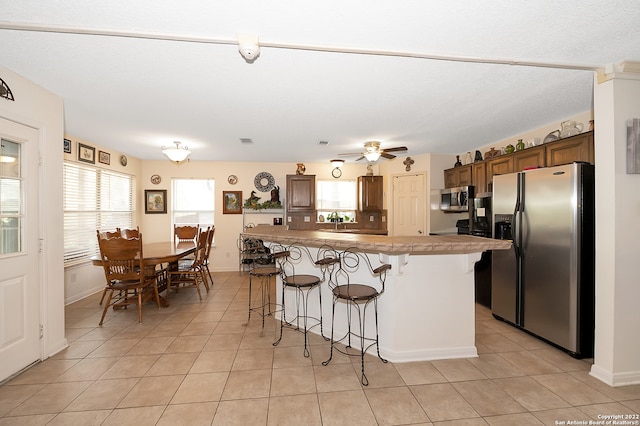 kitchen featuring ceiling fan, light tile patterned floors, stainless steel appliances, a center island, and a breakfast bar area