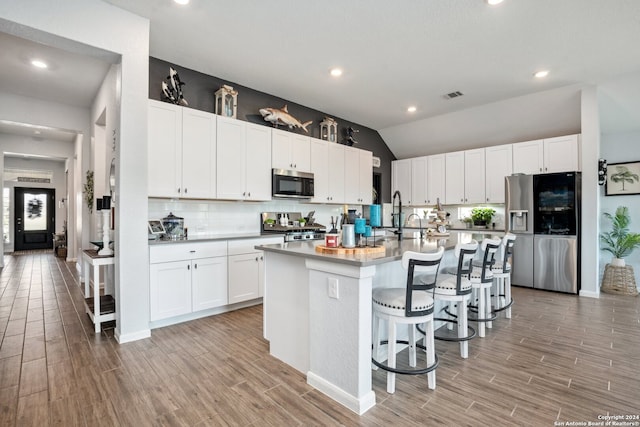 kitchen with white cabinets, lofted ceiling, a center island with sink, light hardwood / wood-style flooring, and stainless steel appliances