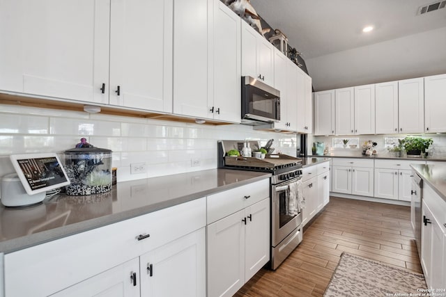 kitchen with stainless steel appliances, backsplash, white cabinets, and hardwood / wood-style flooring