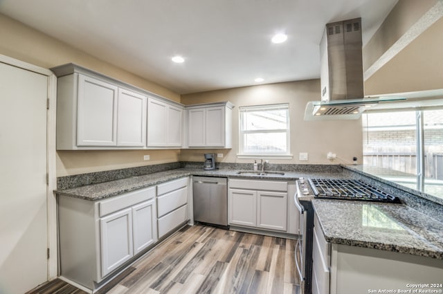 kitchen with sink, dark stone counters, ventilation hood, stainless steel appliances, and light wood-type flooring