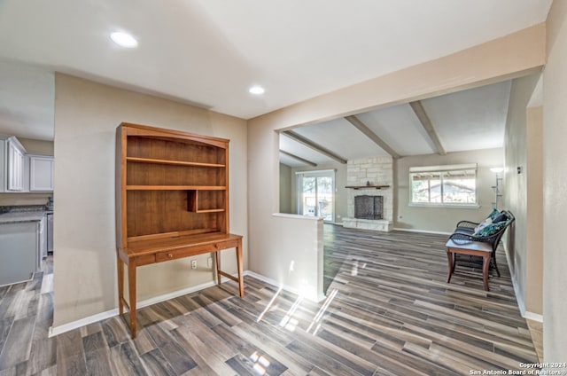 living area featuring vaulted ceiling with beams, dark wood-type flooring, and a stone fireplace