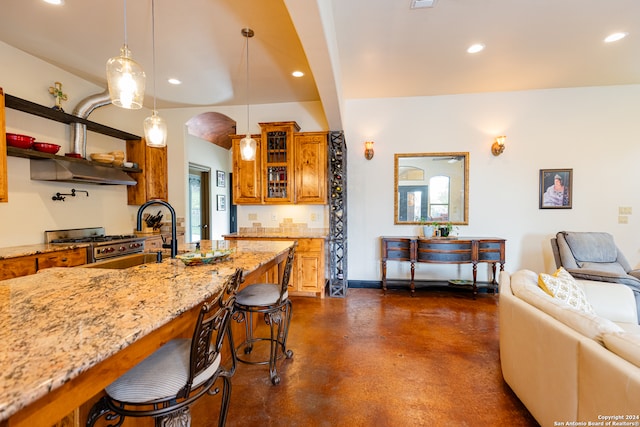 kitchen featuring light stone countertops, exhaust hood, a breakfast bar, stainless steel range oven, and hanging light fixtures