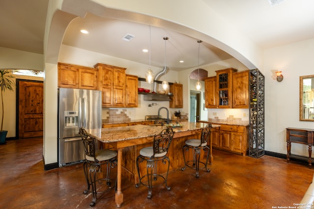 kitchen featuring stainless steel fridge, sink, decorative backsplash, light stone countertops, and hanging light fixtures