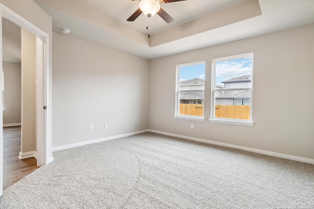 spare room with ceiling fan, a tray ceiling, and carpet