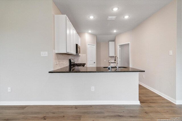 kitchen featuring sink, kitchen peninsula, white cabinets, stainless steel range oven, and dark stone counters