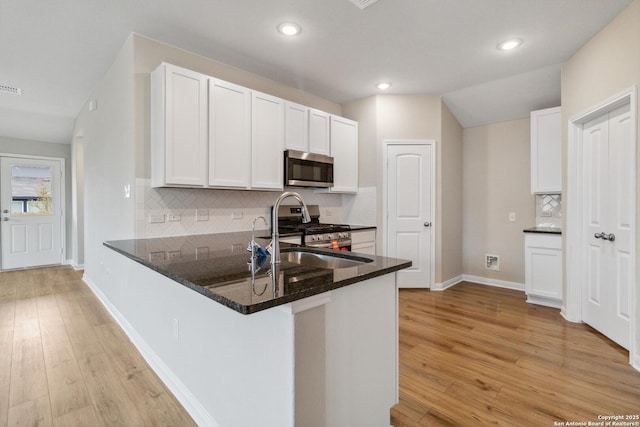 kitchen with white cabinetry, dark stone counters, kitchen peninsula, stainless steel appliances, and light hardwood / wood-style floors