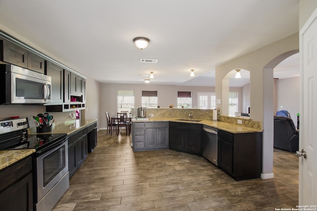 kitchen with dark brown cabinetry, dark hardwood / wood-style flooring, light stone counters, sink, and appliances with stainless steel finishes