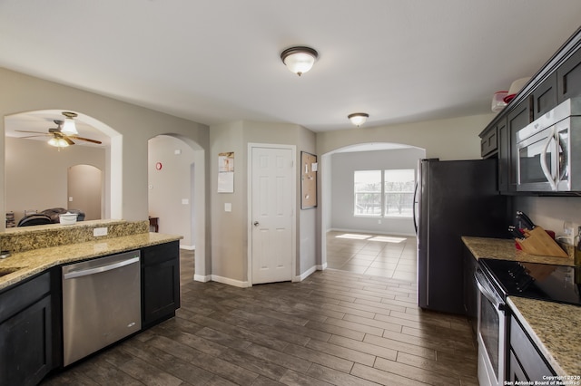 kitchen with stainless steel appliances, dark hardwood / wood-style floors, light stone counters, and ceiling fan