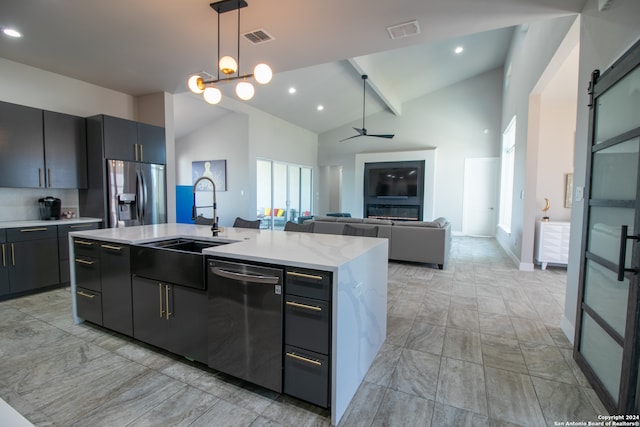 kitchen featuring a barn door, pendant lighting, beam ceiling, a center island with sink, and appliances with stainless steel finishes