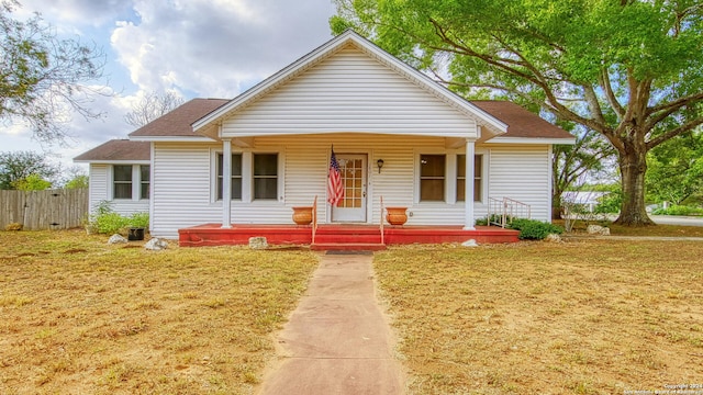 bungalow-style house featuring roof with shingles, fence, a porch, and a front yard