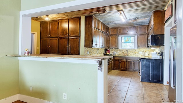 kitchen with light tile patterned floors, stove, sink, decorative backsplash, and kitchen peninsula