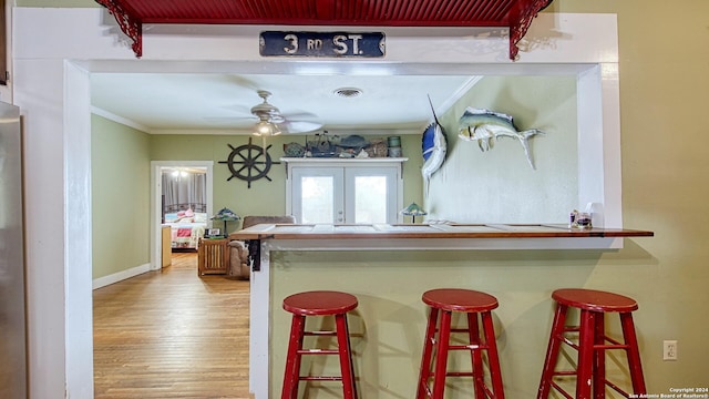 kitchen with french doors, crown molding, light wood-type flooring, a breakfast bar, and ceiling fan