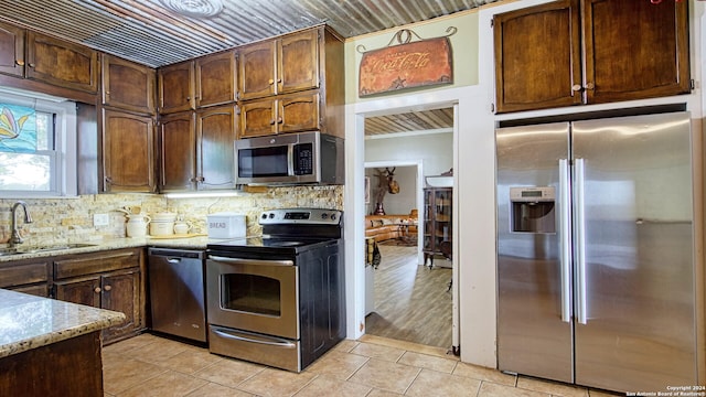 kitchen with stainless steel appliances, sink, light stone countertops, backsplash, and light wood-type flooring