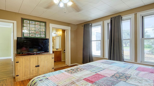 bedroom featuring ensuite bathroom, wood-type flooring, multiple windows, and ceiling fan