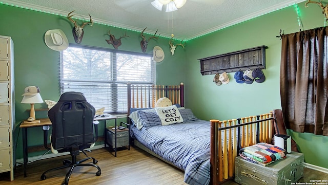 bedroom with a textured ceiling, light wood-type flooring, ornamental molding, and ceiling fan