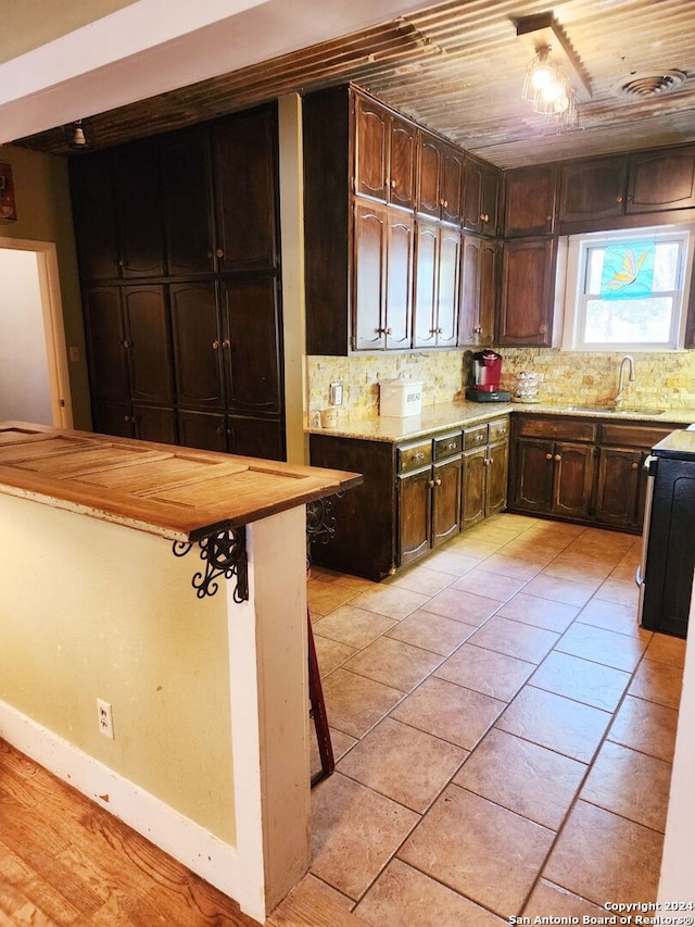 kitchen featuring dark brown cabinetry, butcher block counters, sink, tasteful backsplash, and wood ceiling