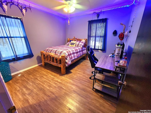 bedroom with multiple windows, wood-type flooring, and ceiling fan