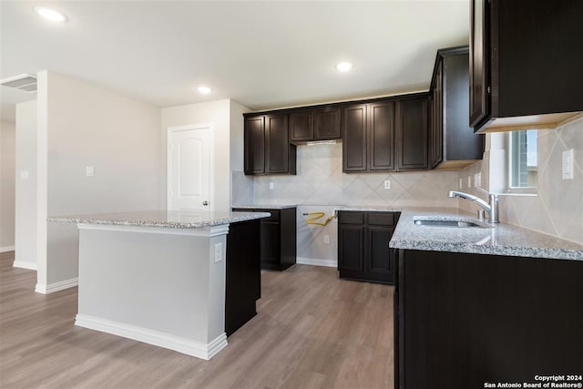 kitchen with light stone counters, sink, a kitchen island, and light wood-type flooring