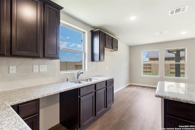 kitchen featuring sink, light hardwood / wood-style flooring, dark brown cabinetry, light stone countertops, and decorative backsplash