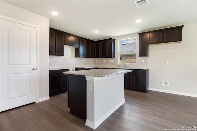 kitchen featuring dark brown cabinetry, dark hardwood / wood-style floors, a center island, and light stone countertops