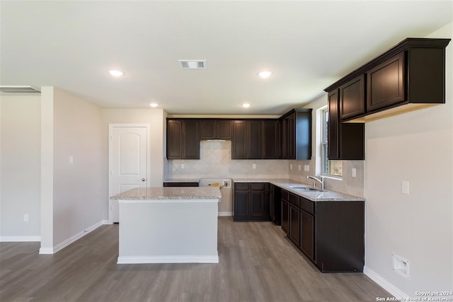 kitchen with dark brown cabinets, a center island, tasteful backsplash, light stone countertops, and light wood-type flooring