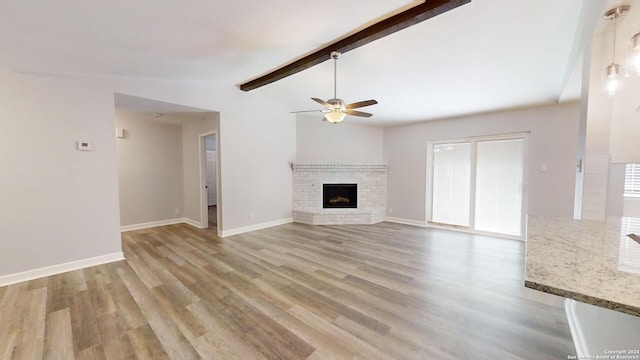 unfurnished living room featuring a brick fireplace, light wood-type flooring, lofted ceiling with beams, and ceiling fan