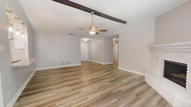 unfurnished living room with ceiling fan, beamed ceiling, light hardwood / wood-style flooring, and a fireplace