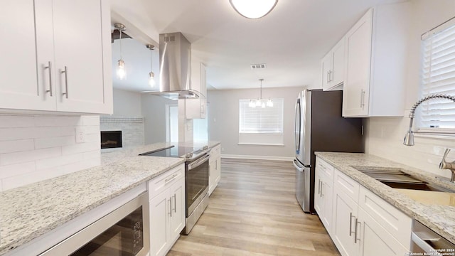 kitchen with wall chimney exhaust hood, pendant lighting, stainless steel appliances, light stone countertops, and white cabinets