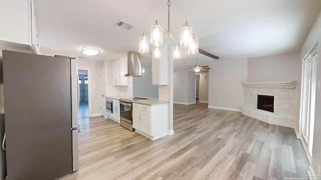 kitchen with light wood-type flooring, white cabinets, pendant lighting, wall chimney range hood, and appliances with stainless steel finishes