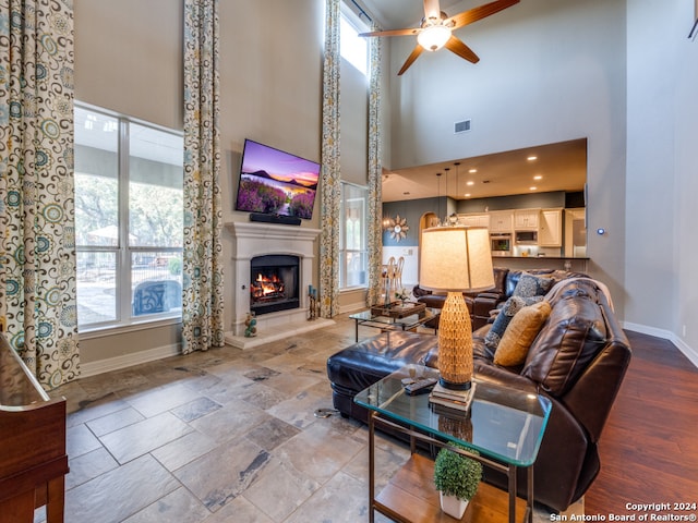 living room with ceiling fan, a healthy amount of sunlight, a towering ceiling, and light hardwood / wood-style flooring