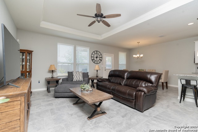 living room with ceiling fan with notable chandelier, crown molding, and a tray ceiling