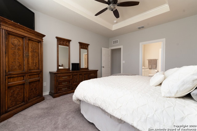 carpeted bedroom with ceiling fan, ensuite bath, and a raised ceiling