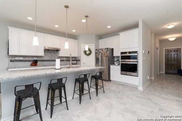 kitchen featuring stainless steel appliances, pendant lighting, white cabinets, and light stone counters