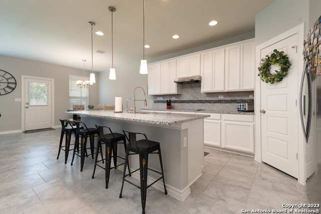 kitchen featuring an island with sink, hanging light fixtures, backsplash, and white cabinets