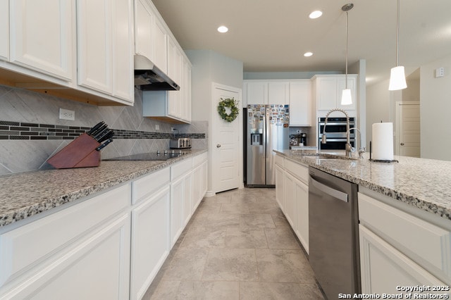 kitchen featuring pendant lighting, tasteful backsplash, light stone counters, stainless steel appliances, and white cabinets