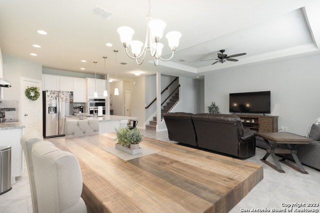 dining area featuring ceiling fan with notable chandelier, a tray ceiling, and light tile patterned floors