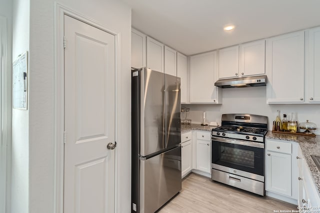 kitchen featuring dark stone countertops, stainless steel appliances, light wood-type flooring, and white cabinetry