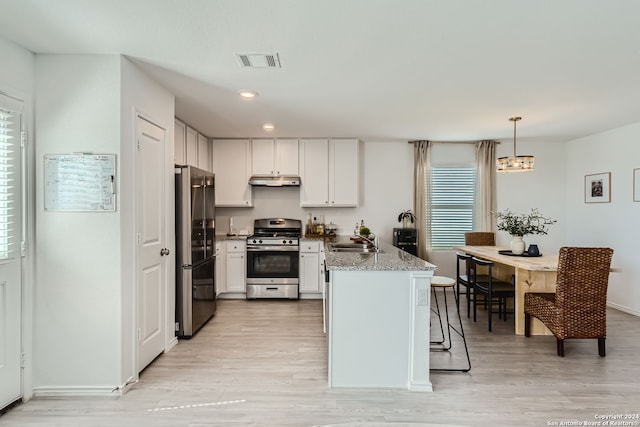 kitchen featuring light wood-type flooring, stainless steel appliances, light stone countertops, hanging light fixtures, and white cabinets