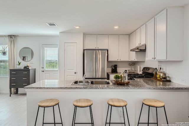 kitchen with white cabinets, black gas stove, light hardwood / wood-style floors, stainless steel refrigerator, and a kitchen bar