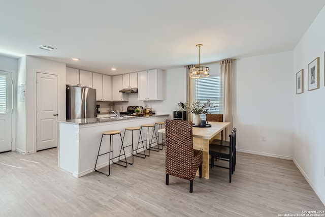 kitchen with stainless steel appliances, pendant lighting, light hardwood / wood-style flooring, and white cabinetry