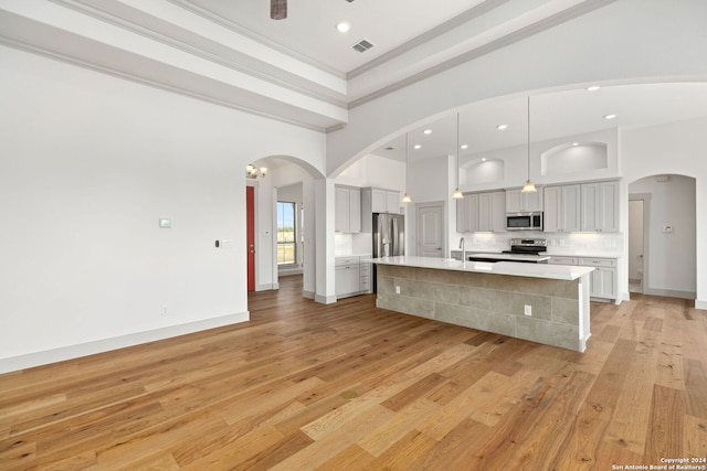 kitchen with light wood-type flooring, pendant lighting, crown molding, stainless steel appliances, and a large island