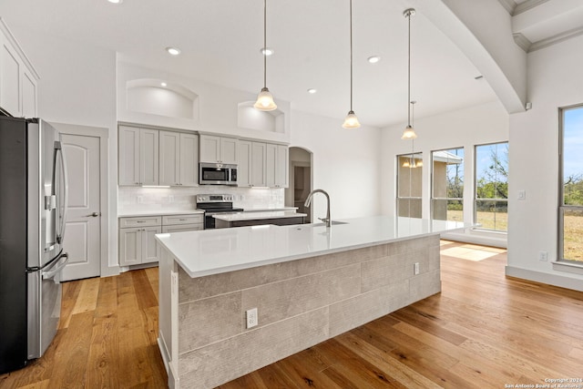 kitchen featuring stainless steel appliances, pendant lighting, a kitchen island with sink, and light wood-type flooring