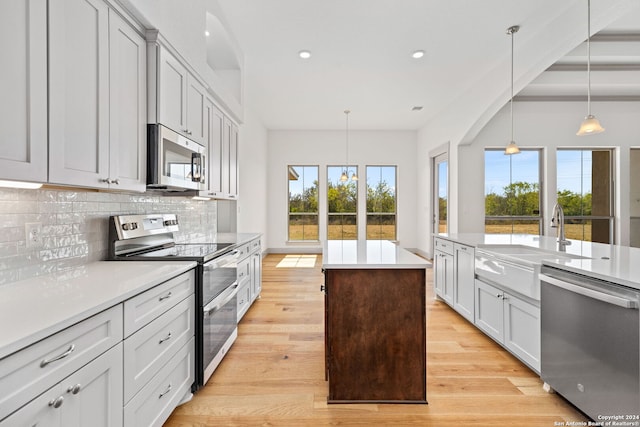 kitchen featuring pendant lighting, stainless steel appliances, a healthy amount of sunlight, and light hardwood / wood-style flooring