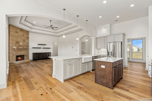 kitchen with sink, decorative light fixtures, a kitchen island with sink, appliances with stainless steel finishes, and light hardwood / wood-style floors