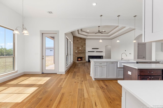 kitchen featuring hanging light fixtures, sink, light hardwood / wood-style flooring, a tray ceiling, and a fireplace