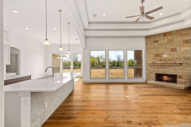 interior space with pendant lighting, sink, a stone fireplace, a large island with sink, and light hardwood / wood-style floors